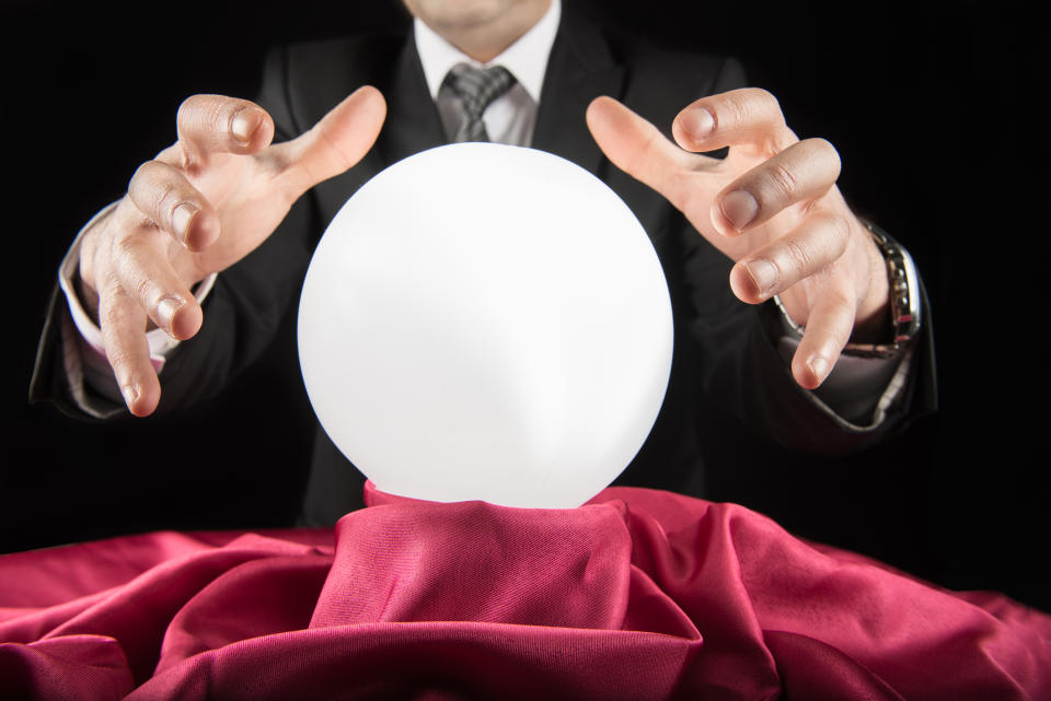 A fortune teller waving his hands above a crystal ball on a table in front of him.