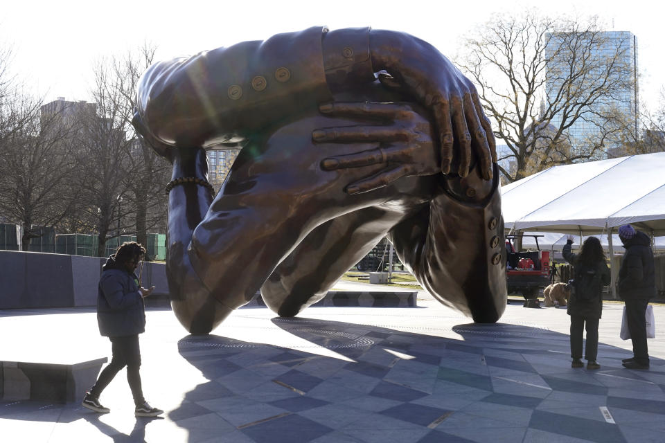 Passers-by walk near the 20-foot-high bronze sculpture "The Embrace," a memorial to Dr. Martin Luther King Jr. and Coretta Scott King, in the Boston Common, Tuesday, Jan. 10, 2023, in Boston. The sculpture, consisting of four intertwined arms, was inspired by a photo of the Kings embracing when MLK learned he had won the Nobel Peace Prize in 1964. The statue is to be unveiled during ceremonies Friday, Jan. 13, 2023. (AP Photo/Steven Senne)