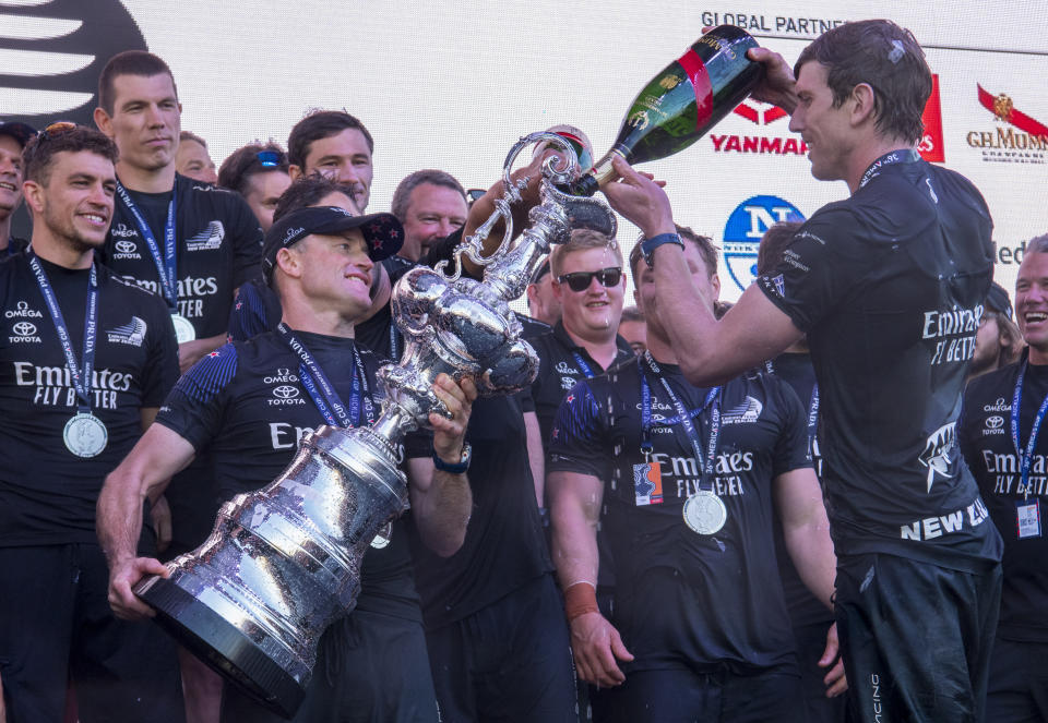 Emirates Team New Zealand helmsman Peter Burling, right, pours champagne into the America's Cup trophy after defeating Italy's Luna Rossa in race ten of the America's Cup on Auckland's Waitemata Harbour, Wednesday, March 17, 2021.Team New Zealand has retained the America's Cup by beating Italian challenger Luna Rossa 7-3 in the 36th match for sailing's oldest trophy. (Chris Cameron/Photosport via AP)