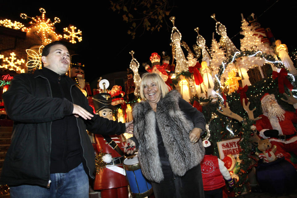 This Dec. 4, 2012 photo shows Lucy Spata outside her decorated home with tour guide Tony Muia in the Brooklyn borough of New York. Each holiday season, tour operator Muia takes tourists from around the world on his “Christmas Lights & Cannoli Tour” visiting the Brooklyn neighborhoods of Dyker Heights and Bay Ridge, where locals take pride in over-the-top holiday light displays. (AP Photo/Seth Wenig)