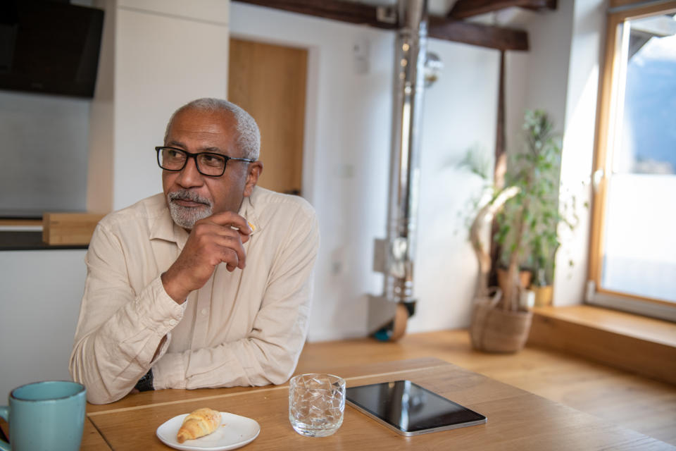 A person sitting at a table with a pastry and a tablet, looking pensively out a window