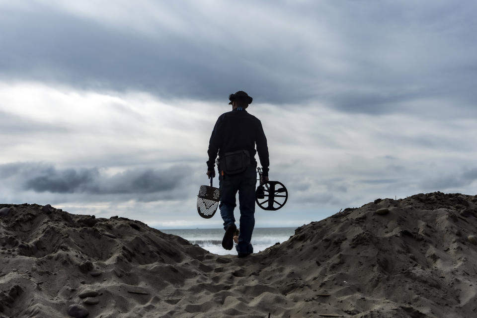 Metal detectorist Josh Snider walks over a sand mound to search for metals on the edge of the beach ahead of storms, Wednesday, Jan. 31, 2024, in Ventura, Calif. The first of two back-to-back atmospheric rivers slowly pushed into California on Wednesday, triggering statewide storm preparations and calls for people to get ready for potential flooding, heavy snow and damaging winds. (AP Photo/Damian Dovarganes)