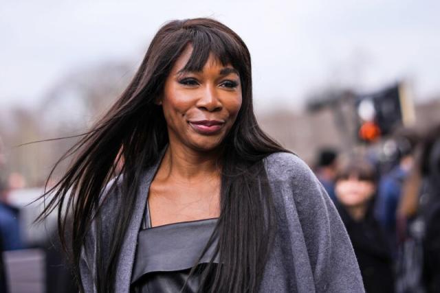 Venus Williams wears a black shiny leather dress and a pale gray wool coat during Paris Fashion Week