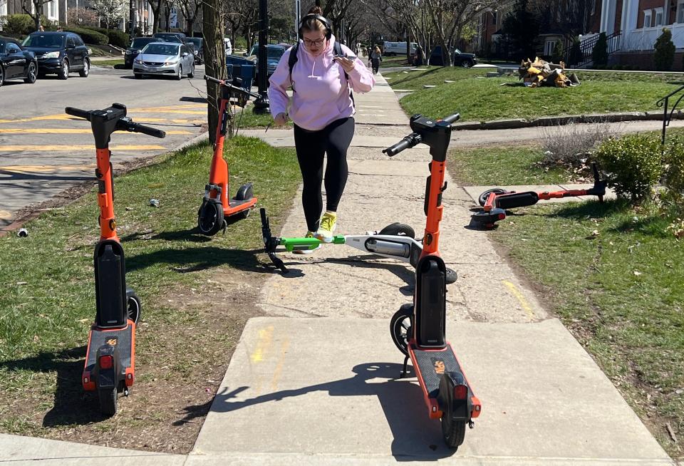 A student steps over the Spin and Lime scooters left on an E. 15th Ave sidewalk in the off-campus area of Ohio State University Thursday, March 28, 2024.