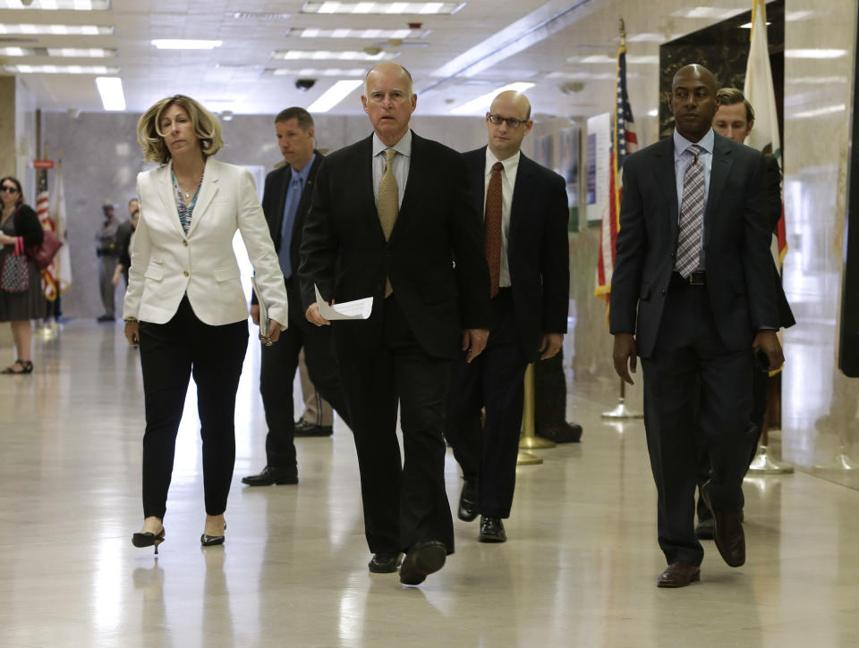 In this photo taken Tuesday, May 13, 2014, Gov. Jerry Brown, center, walks to a news conference to unveil his revised 2014-15 state budget at the Capitol in Sacramento, Calif. Brown is facing Republican challengers, Assemblyman Tim Donnelly and businessman Neel Kashkari, in his bid to win reelection this year.(AP Photo)