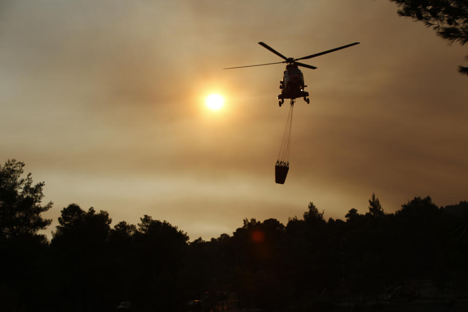 A firefighting helicopter approaches a lake to load water, as it participates in an operation against, a wildfire in northern Athens, Saturday, Aug. 7, 2021. Wildfires rampaged through Greek forests for yet another day Saturday, threatening homes and triggering more evacuations a day after hundreds of people were plucked off beaches by ferries in a dramatic overnight rescue. (AP Photo/Lefteris Pitarakis)