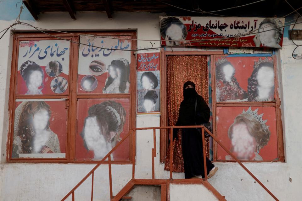 2021年10月6日，阿富汗喀布爾，一名穿罩袍的婦女進入一家美容院，店外海報上的女性臉孔都已被塗掉。路透社