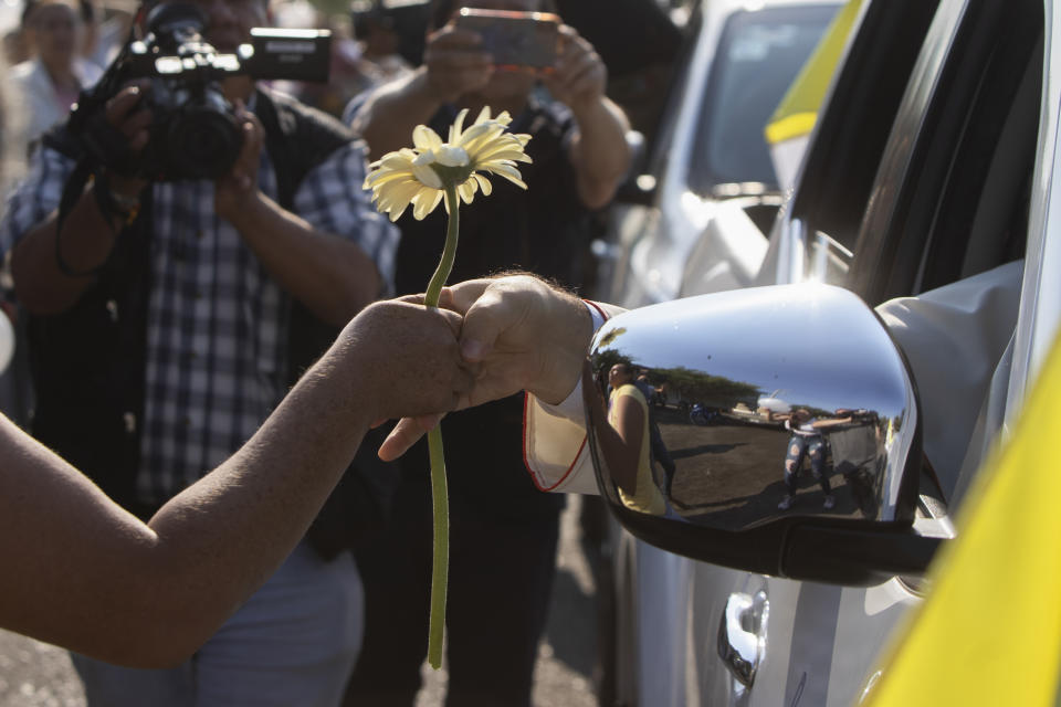 Monsignor Franco Coppola, the Vatican's diplomat to Mexico, receives a flower as he arrives to meet families and celebrate Mass in Aguililla, a town that has been cut off by warring cartels in Michoacan state, Mexico, Friday, April 23, 2021. State police and soldiers were sent in to restore order earlier this month, but cartels responded by parking hijacked trucks across roads to block them, as well as digging deep trenches across roadways. (AP Photo/Armando Solis)