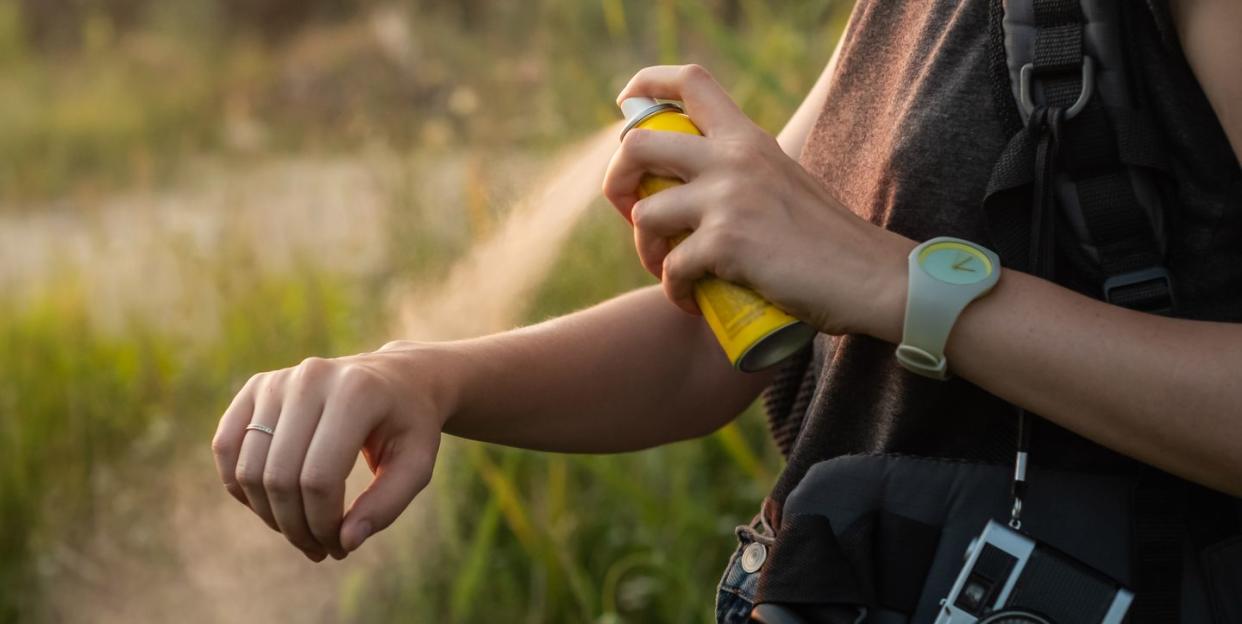 close up of young female backpacker tourist applying bug spray on hands