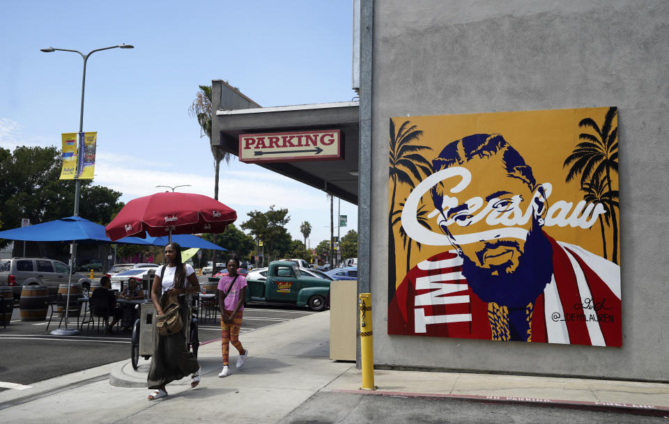 Pedestrians walk past a street mural of the late rapper Nipsey Hussle, Thursday, June 30, 2022, in the Crenshaw district of Los Angeles. The many murals of Hussle around Los Angeles speak to the late rapper's lasting legacy. (AP Photo/Chris Pizzello)