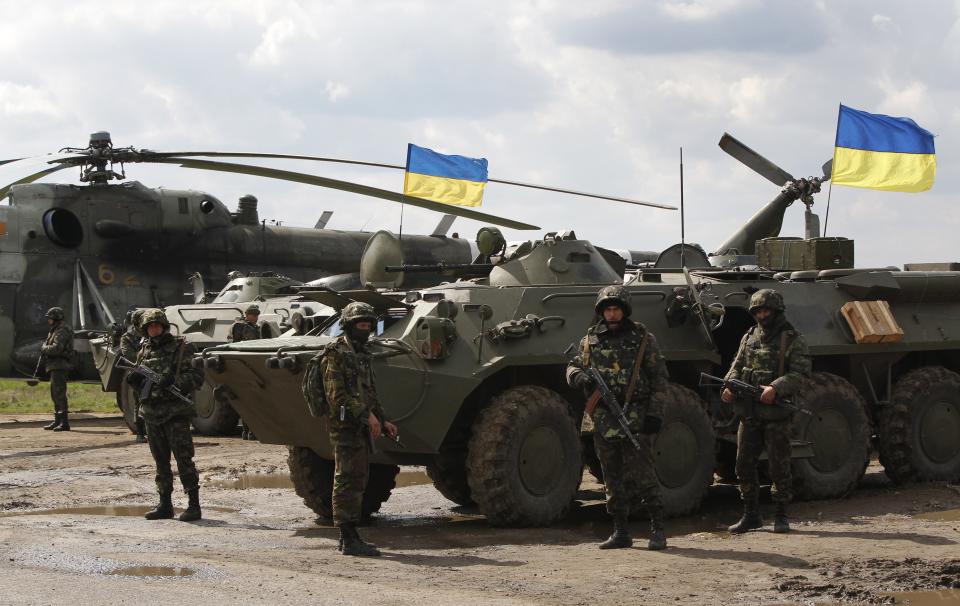 Ukrainian soldiers stand at APCs, with Ukrainian flags in the back, as Ukrainian army troops receive ammunition in a field on the outskirts of Izyum, Eastern Ukraine, Tuesday, April 15, 2014. An Associated Press reporter saw at least 14 armored personnel carriers with Ukrainian flags, one helicopter and military trucks parked 40 kilometers (24 miles) north of the city on Tuesday. (AP Photo/Sergei Grits)