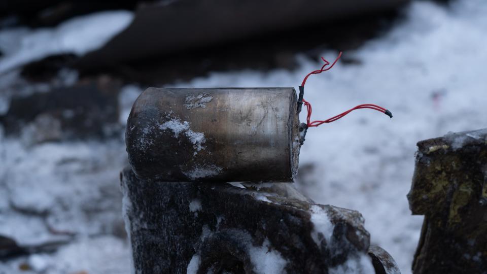 A missile fragment with red wires sticking out of it. A snowy ground is in the background.