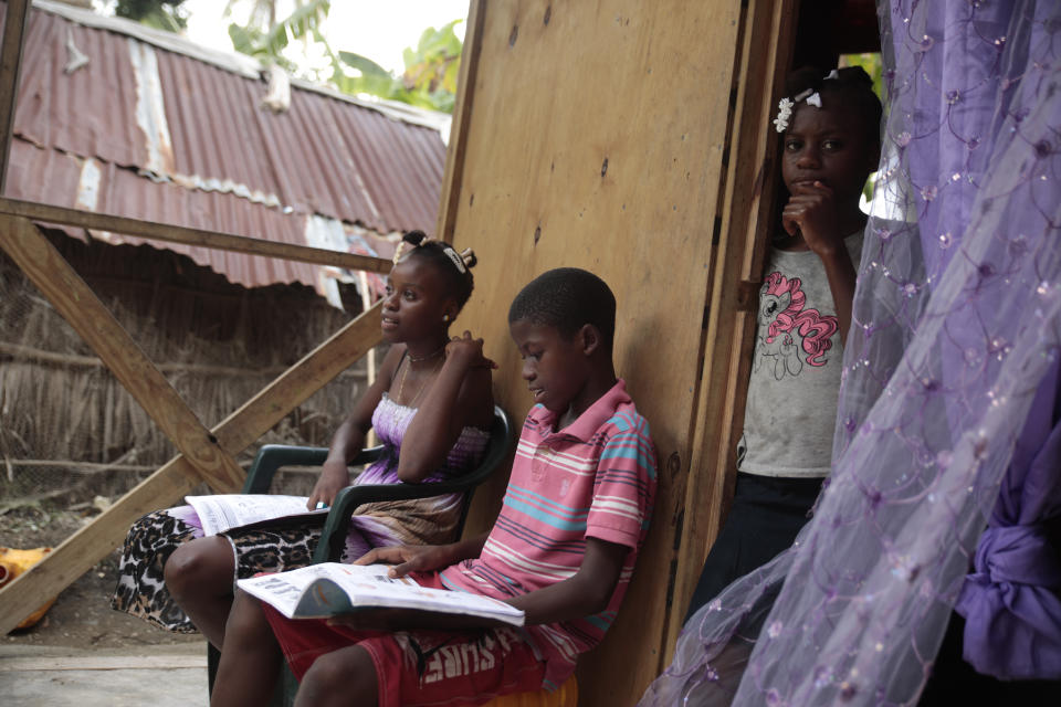 Los hermanos Mylouise Veillard, a la izquierda, y Myson estudian junto a su hermana Routcheland, de pie en la entrada de su casa en una zona rural de Saint-Louis-du-Sud, Haití, el jueves 25 de mayo de 2023. , Thursday, May 25, 2023. Mylouise y Myson estuvieron considerados como "huérfanos de pobreza" durante tres años hasta que se reunieron con su madre, Renèse Estève, que les había dejado en orfanato donde creía que estarían mejor atendidos. Su madre se los llevó a casa tras asustarse por el peso que habían perdido, convencida de que estarían mejor en la pobreza extrema. (AP Foto/Odelyn Joseph)