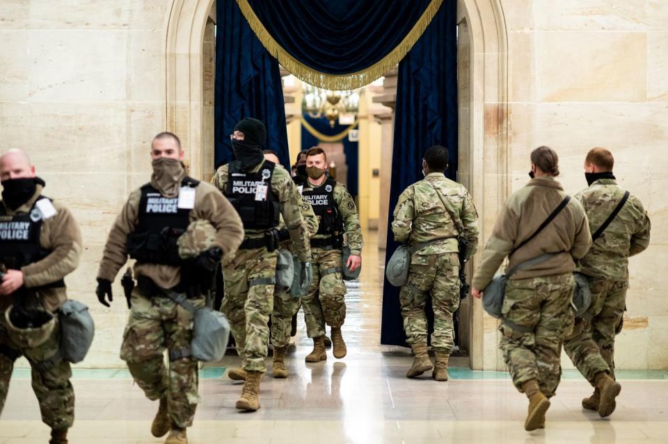 <p>National Guard troops walk through a doorway on the first floor of the Capitol decorated for the Inauguration on Wednesday, Jan. 13, 2021</p>