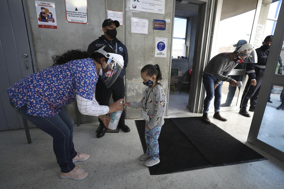 A teacher gives anti-bacterial gel to a preschool student on the first day back to in-person class amid the COVID-19 pandemic in Bogota, Colombia, Monday, Feb. 15, 2021. Bogota is returning students to blended classes at public schools after a year of online education due to the pandemic. (AP Photo/Fernando Vergara)