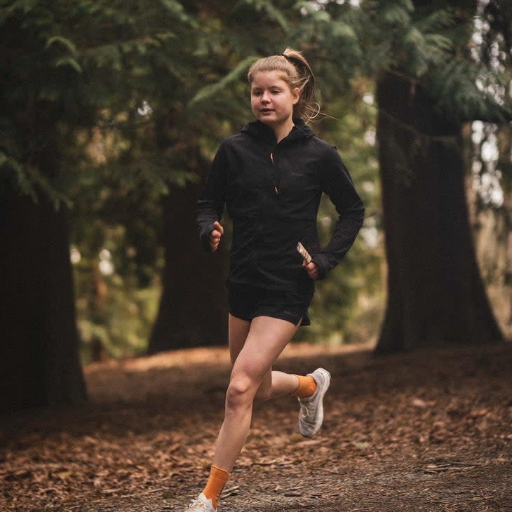 Elite runner Allie Ostrander runs in the forest with a black jacket