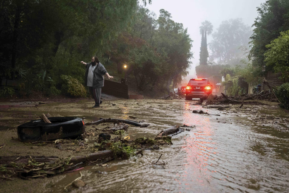 A resident attempts to help a vehicle stuck on Fredonia Drive in Studio City, Calif., where a mudslide is blocking the road during a rain storm on Tuesday, Jan. 10, 2023. California saw little relief from drenching rains as the latest in a relentless string of storms swamped roads, turned rivers into gushing flood zones and forced thousands of people to flee from towns with histories of deadly mudslides.(Sarah Reingewirtz /The Orange County Register via AP)