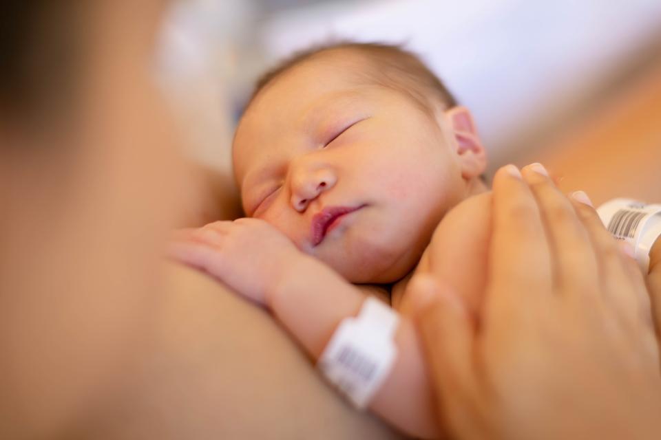 A mother holding her newborn baby on her warm chest for skin on skin time at the hospital. Umbilical cord blood banking