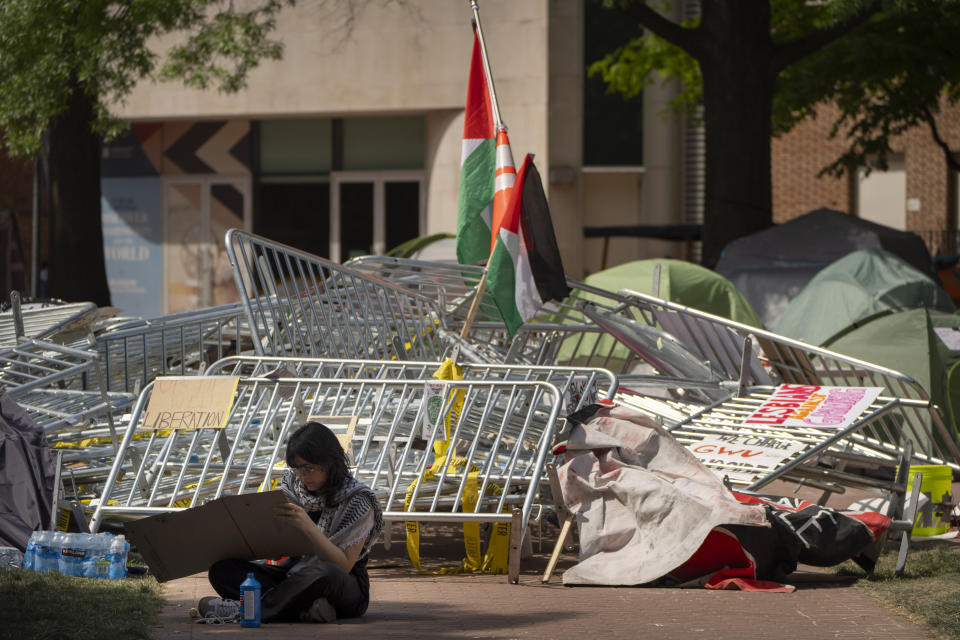 Una persona hace un letrero mientras está sentada cerca de un montón de barricadas en un campamento de protesta contra la guerra entre Israel y Hamás en la Universidad George Washington, el martes 30 de abril de 2024, en Washington. (AP Foto/Mark Schiefelbein)