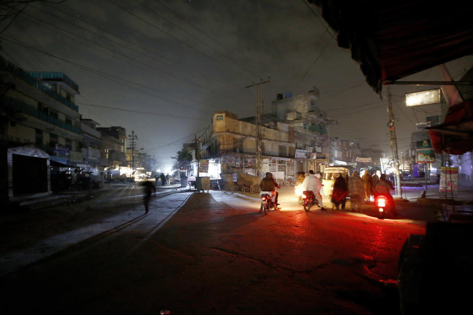 People are silhouetted on vehicles headlights on a dark street during widespread power outages in Rawalpindi, Pakistan, Sunday, Jan. 10, 2021. Pakistan's national power grid experienced a major breakdown late night on Saturday, leaving millions of people in darkness, local media reported. (AP Photo/Anjum Naveed)