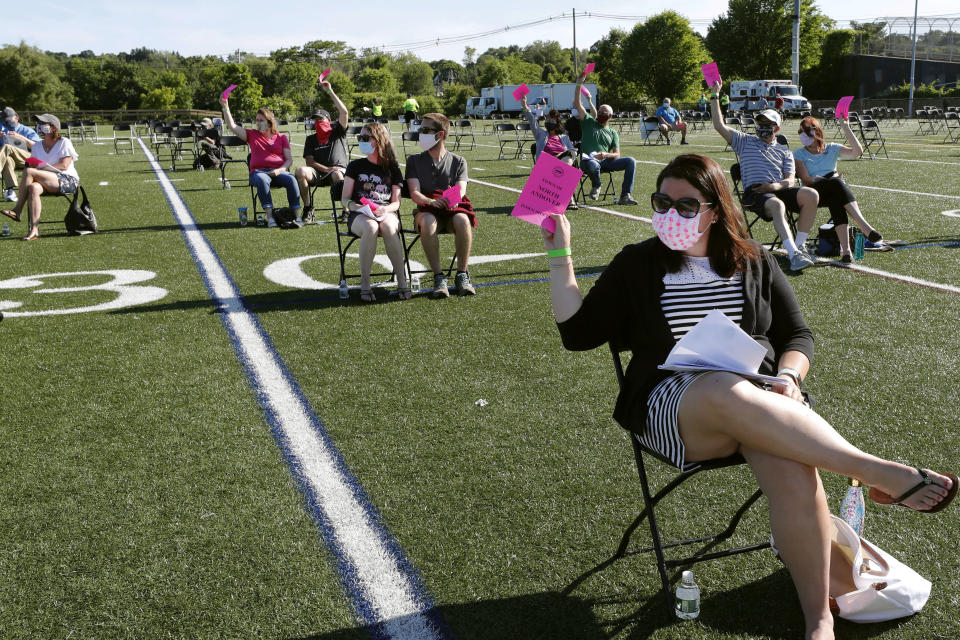 FILE - In this June 16, 2020, file photo, residents hold up pink cards to vote on an issue during the annual town meeting held at the high school football field to provide social distancing due to COVID-19 concerns, in North Andover, Mass. It was the first town meeting held outdoors since town meetings began in North Andover in 1646. (AP Photo/Elise Amendola, File)