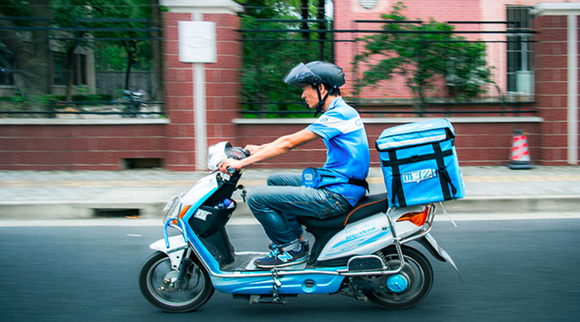 An Ele.me delivery employee rides a scooter to deliver food to a customer.