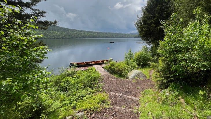 A wooden canoe docked at the end of a lake pier, with steps leading down to it