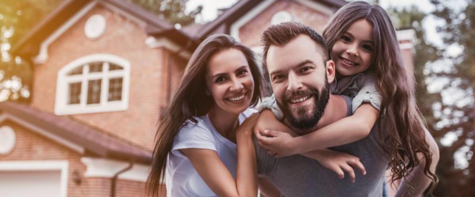 Happy family is standing near their modern house, smiling and looking at camera.