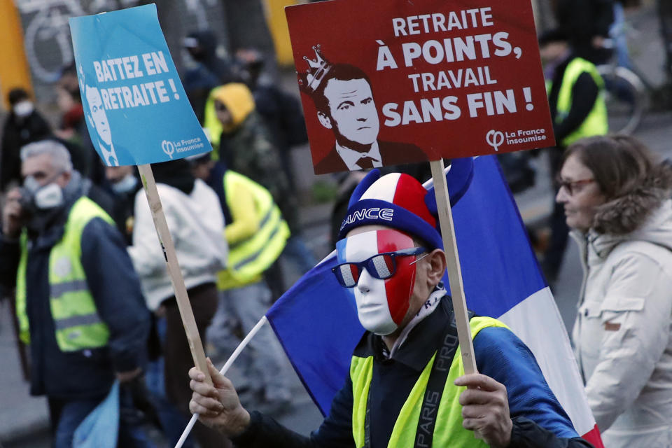 A protester holds a banner with French President Emmanuel Macron reading "Pensions with points, never ending work" during a demonstration, Saturday, Jan. 11, 2020 in Paris. The French government and labor unions appeared far from reaching any compromise deal Friday in talks over a planned pension overhaul, with strikes and protests grinding on. (AP Photo/Francois Mori)