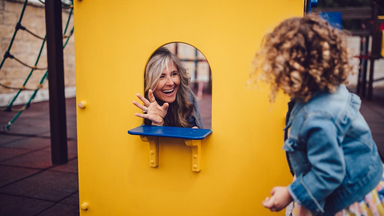 Happy retired grandmother and little granddaughter having fun playing make believe game together at playground.