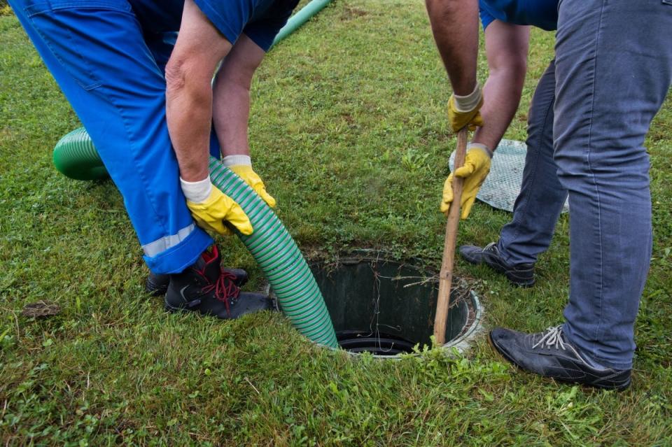 Two people pumping septic system using a long green hose