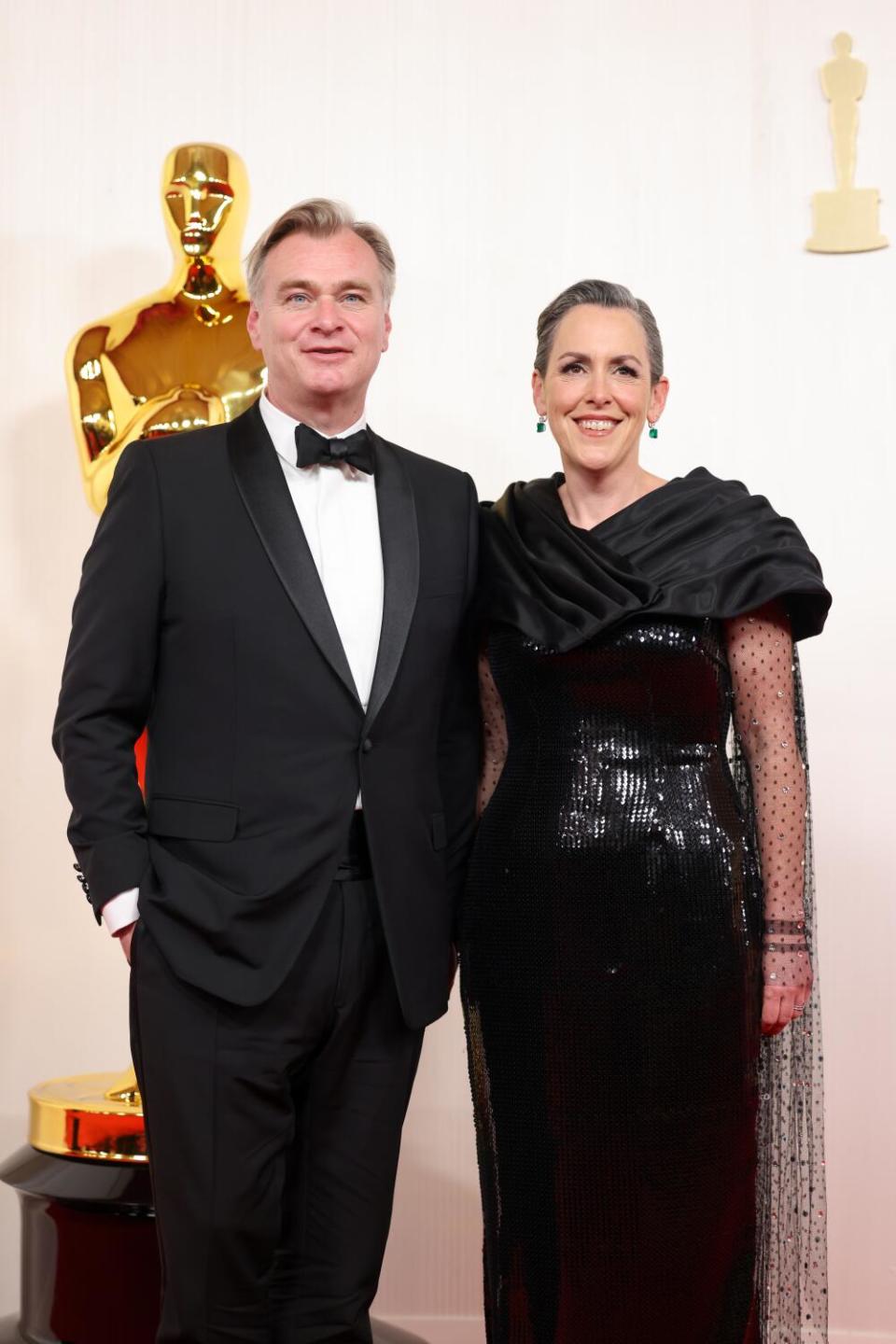 Christopher Nolan and Emma Thomas, in black, pose in front of an Oscar statue.