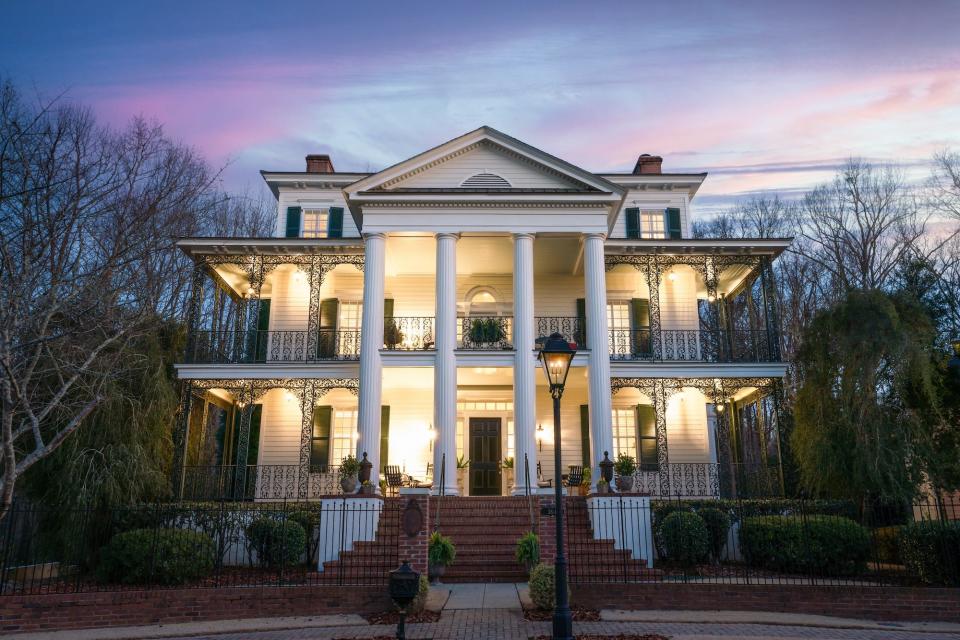 A large, white mansion lit up at sunset.