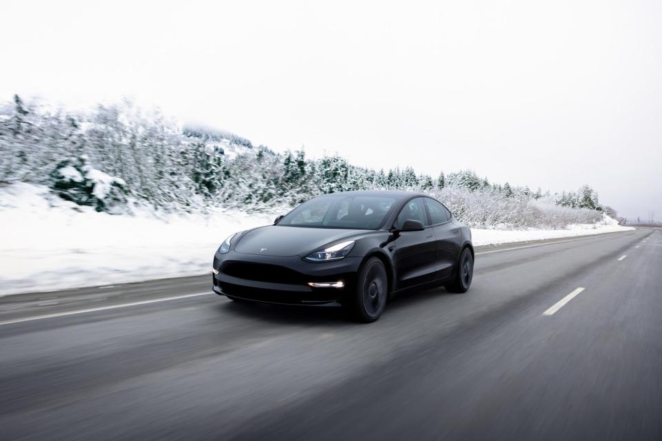 An all-electric Model 3 sedan driving down a highway during wintry conditions.