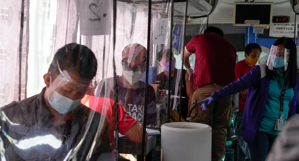 People wait inside a bus used as a mobile Covid-19 vaccination centre to encourage people to get inoculated in Taguig, Philippines on Saturday June 18, 2021. Source: AAP