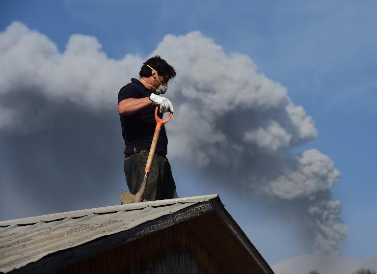 A man cleans the roof of a house in La Ensenada, Chile, with the Calbuco volcano in the background, April 24, 2015