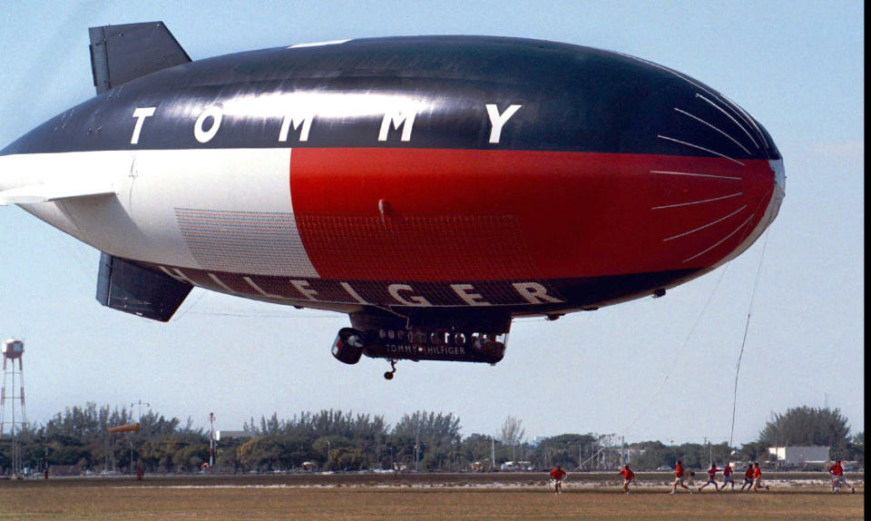 FILE - In this Jan. 25, 1999 file photo, ground crew scramble to catch the lines and guide the Tommy Hilfiger Airship to a smooth landing at North Perry Airport, in Pembroke Pines, Fla. The blimp was in town for the Super Bowl. Sports economists say the financial impact of the Super Bowl could fall far below expectations, in part because visitors often spend their cash at NFL-sponsored or corporate events rather than at tourist attractions. (AP Photo/The Miami Herald,Emily Kelsey, File) MAGS OUT