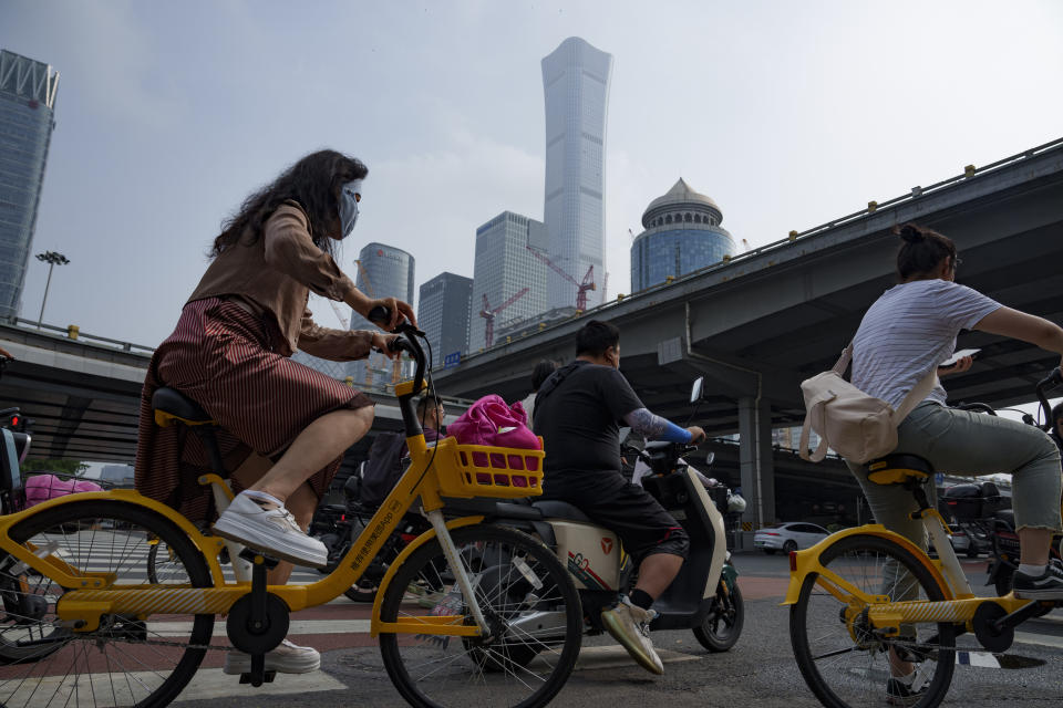 People on bicycle and bike cross an intersection with the background of the central business district in Beijing, China, Monday, July 15, 2024. China's ruling Communist Party is starting a four-day meeting Monday that is expected to lay out a strategy for self-sufficient economic growth in an era of heightened national security concerns and restrictions on access to American technology. (AP Photo/Vincent Thian)