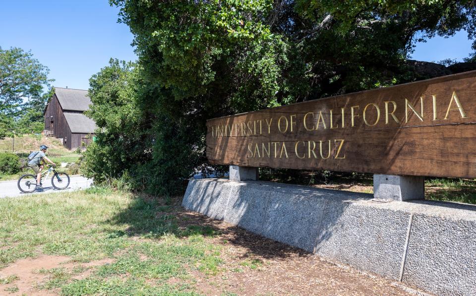A bicyclist rides near the wooden University of California Santa Cruz sign in Santa Cruz, Calif, on Friday, May 22, 2020. 