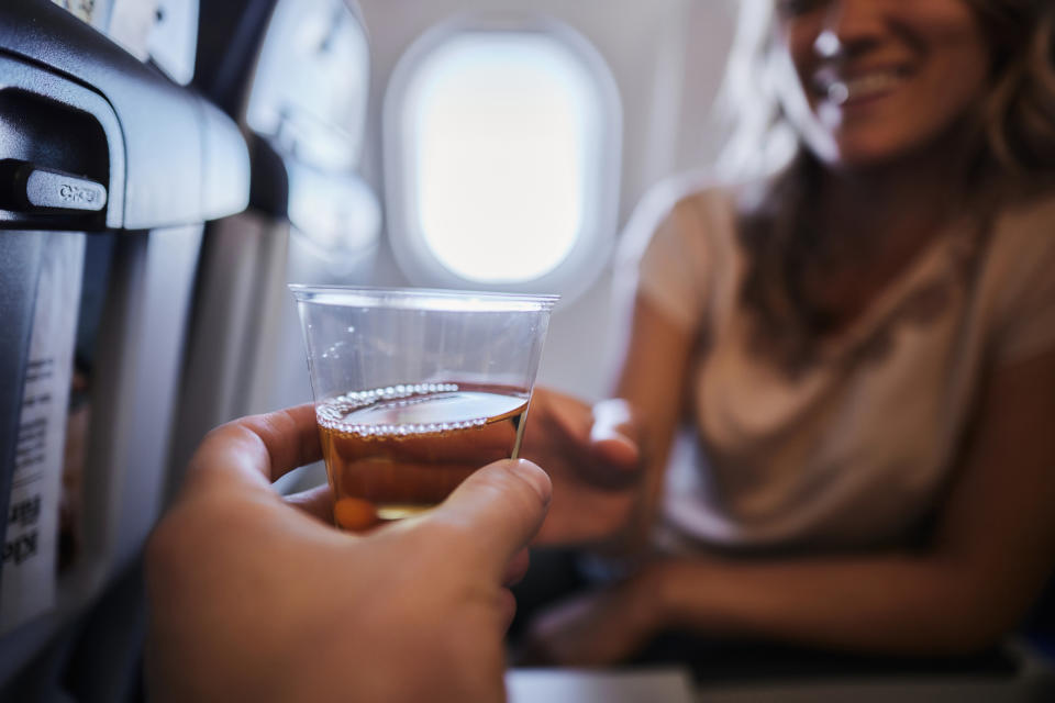 A person hands a drink in a plastic cup to another person on an airplane as they smile in their seat