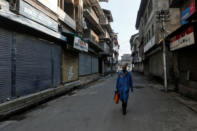 Paramedic walks through a deserted street during curfew ahead of the first anniversary of the revocation of Kashmir's autonomy in Srinagar