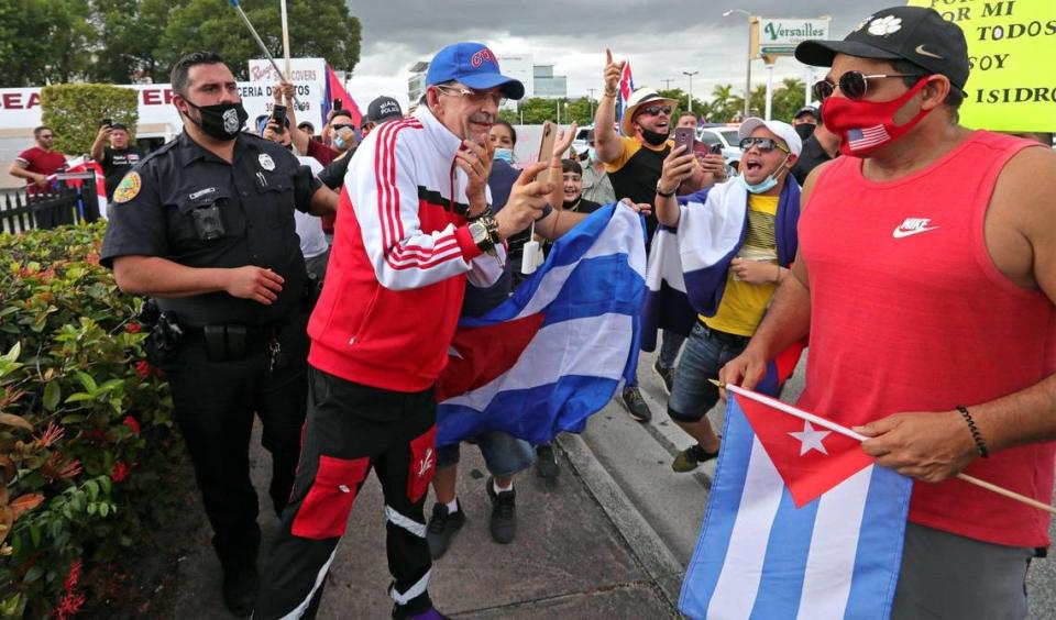 A counter protestor, wearing blue cap, is shouted down as he is escorted by Miami Police during a rally in front of Versailles Restaurant in Miami in support of Cuban artists arrested in Cuban on Saturday, November 28, 2020.