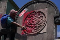 A demonstrator uses red spray paint to symbolize blood over a national symbol outside a military base in Mexico City, Friday, Sept. 23, 2022, days before the anniversary of the 2014 disappearance of 43 college students in Iguala, Guerrero. The sign reads in Spanish "We're missing 43!" One week prior, Mexican authorities said they arrested a retired general and three other members of the army for alleged connection to their disappearance. (AP Photo/Fernando Llano)