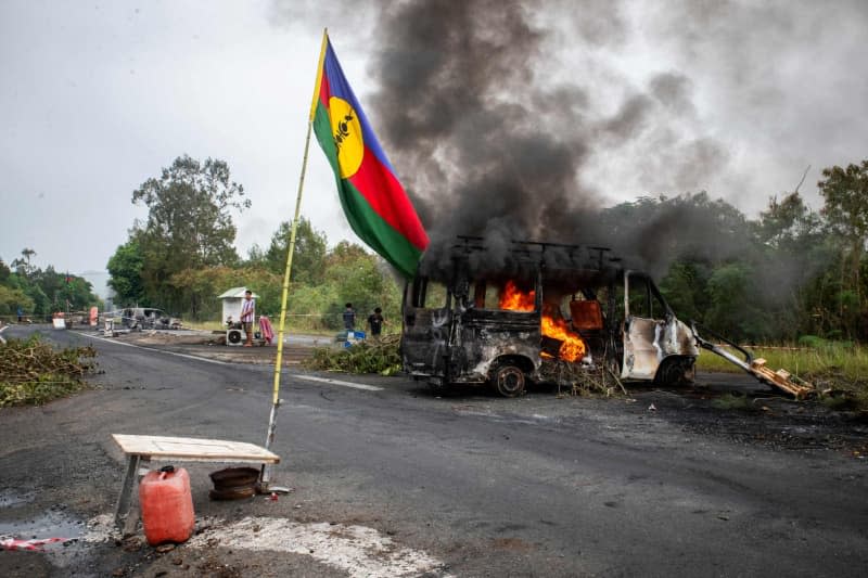 A Kanak flag waves next to a burning vehicle at an independantist roadblock at La Tamoa. The capital of the French Pacific territory of New Caledonia was rocked by riots after France's National Assembly approved contentious voting reforms to the territory that angered independence supporters. Delphine Mayeur/AFP/dpa