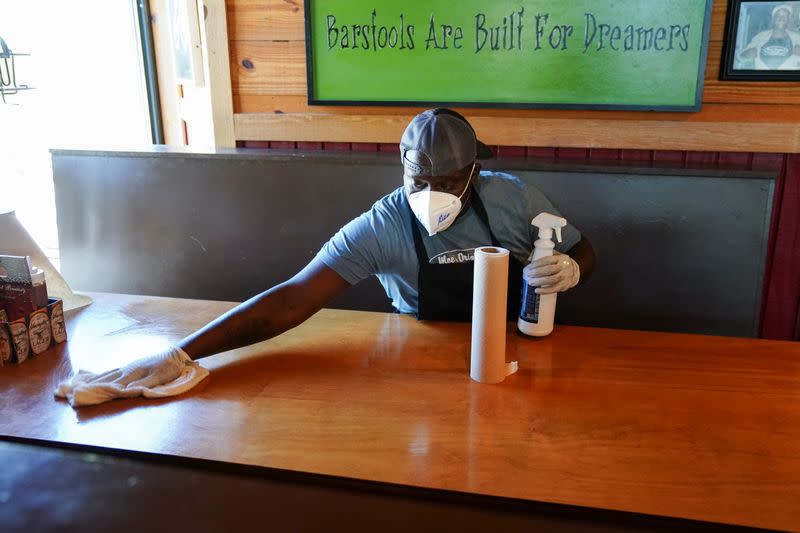 Rico Forde cleans a table after a group of patrons at lunch on it at Moe's Original BBQ after it reopened to the public as part of the phased reopening of businesses from the coronavirus disease rules in Atlanta