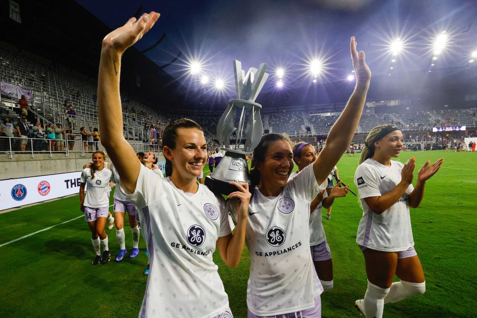 Cece Kizer and Sinclaire Miramontez carry the winner's trophy after Racing Louisville FC won The Women's Cup Championship at their home Lynn Family Stadium.