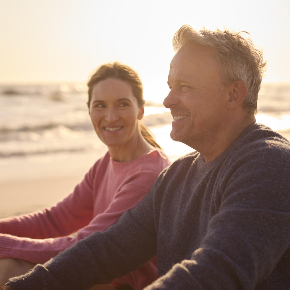 Two people smiling and sitting close together on the beach, suggesting a romantic connection