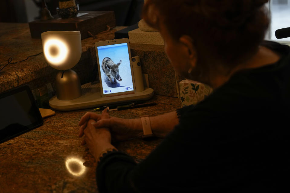 Deanna Dezern, 83, interacts with her ElliQ, a tabletop device that uses artificial intelligence to conduct human-like conversations, inside her home in Tamarac, Fla., Thursday, Dec. 7, 2023. Dezern is among the first in the country to receive the robot ElliQ, whose creators, Intuition Robotics, and senior assistance officials say is the only device using artificial intelligence specifically designed to lessen the loneliness and isolation experienced by many older Americans. (AP Photo/Rebecca Blackwell)