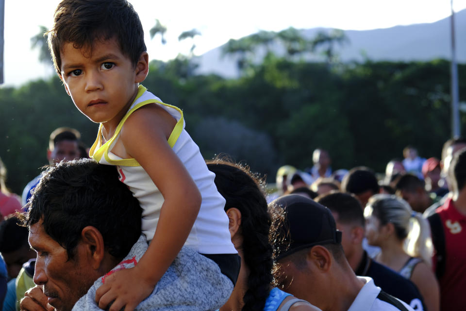 A Venezuelan man carrying a child on his shoulders lines up to cross the Simon Bolivar international bridge into Cucuta, Colombia, Saturday, June 8, 2019. Venezuela's President Nicolas Maduro ordered the partial re-opening of the border that has been closed since February when he stationed containers on the bridge to block an opposition plan to deliver humanitarian aid into the country. (AP Photo/Ferley Ospina)