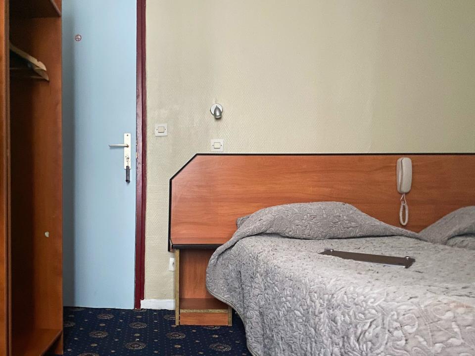 A hotel room with a shelf and door on the left and a bed on the right
